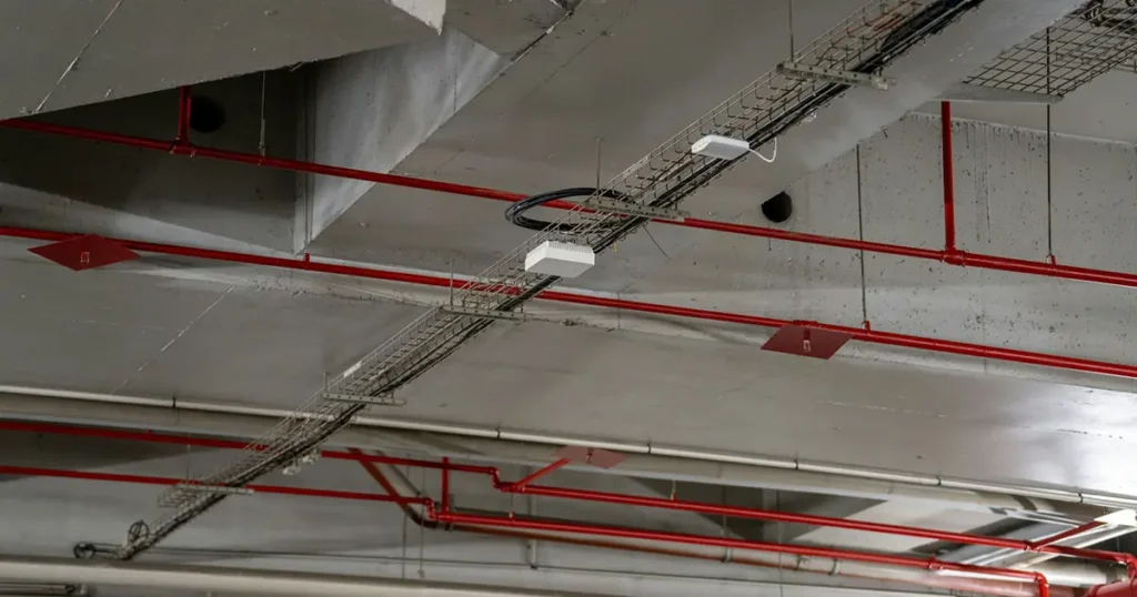 Hammer drive anchors suspending wire mesh cable trays and fire sprinkler pipes from concrete ceiling