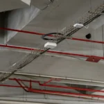 Hammer drive anchors suspending wire mesh cable trays and fire sprinkler pipes from concrete ceiling