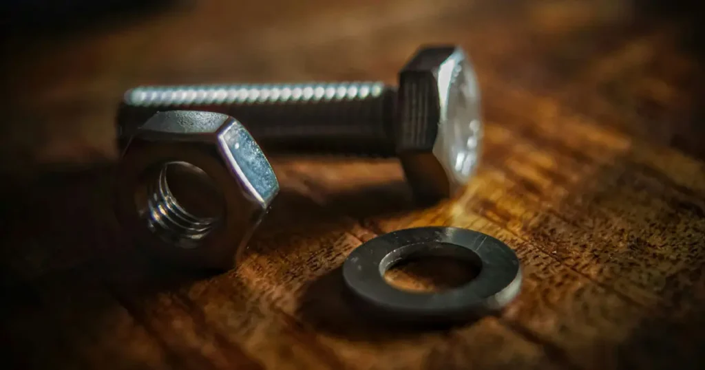 Stainless steel hex bolt nut and washer set on wooden background for mechanical assembly