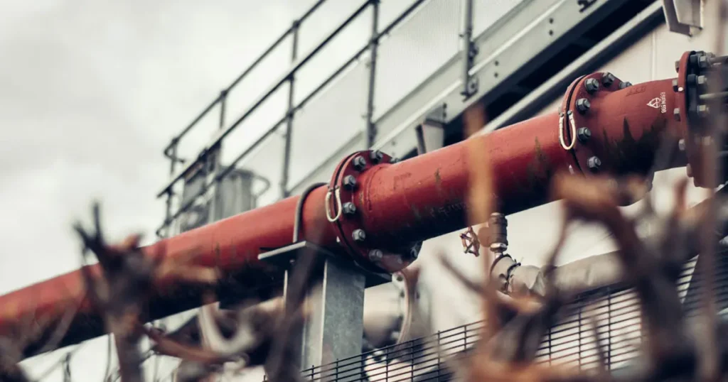 Stainless steel U bolt fasteners securing a red industrial pipeline to its support structure, shown from a low angle, with detailed threads visible