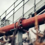 Stainless steel U bolt fasteners securing a red industrial pipeline to its support structure, shown from a low angle, with detailed threads visible