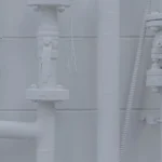 Galvanized steel U-bolt fasteners securing various vertical and horizontal white industrial pipes against a brick wall