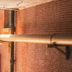 Galvanized U-bolt clamp securing large industrial pipe to wall bracket support