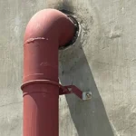 Steel pipe clamp bracket secured with anchor bolt on concrete wall for industrial plumbing system