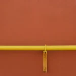 Close-up detail of a painted yellow U-bolt clamp securing a horizontal gas pipeline section to a metal support bracket on a terracotta-colored industrial wall